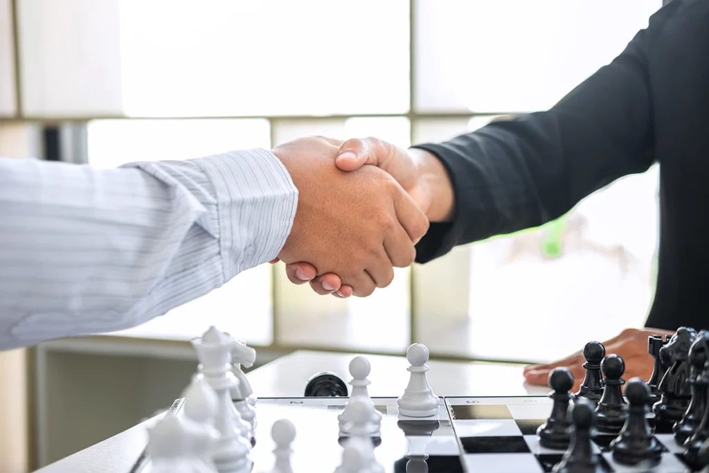 Two people shaking hands over a chessboard